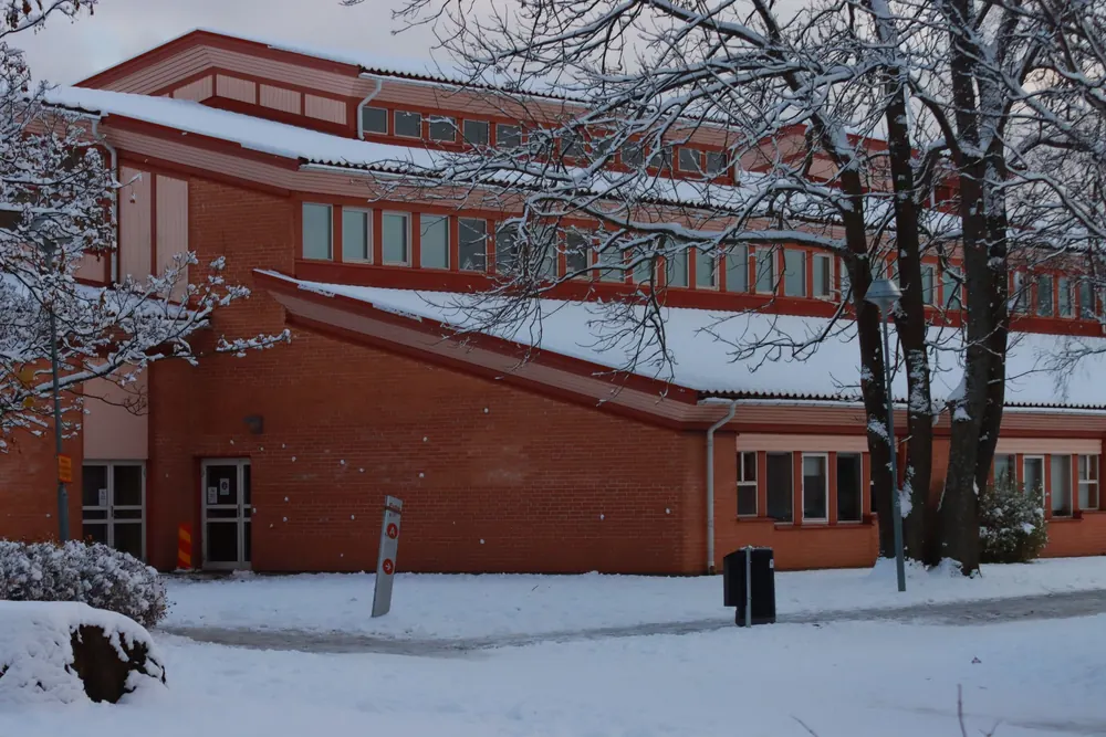 Rote Klinkerbauten einer Wohnanlage im Schnee, davor ein verschneiter Platz und kahle Bäume